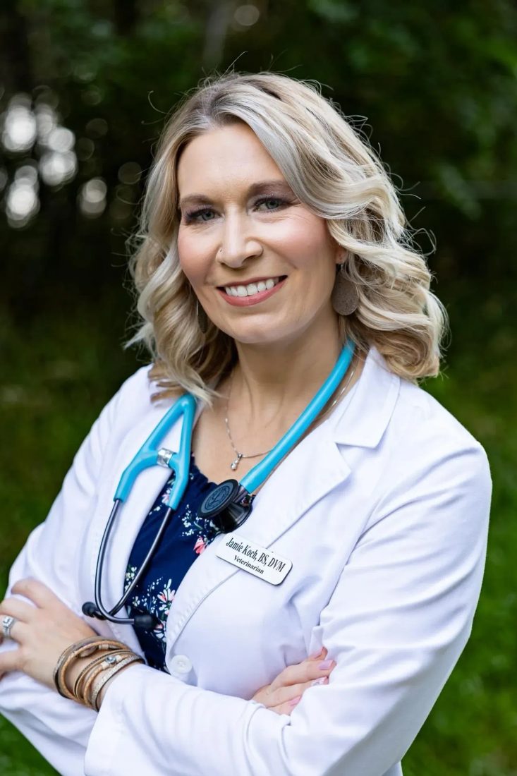 Blonde female veterinarian in white coat with stethoscope outdoors