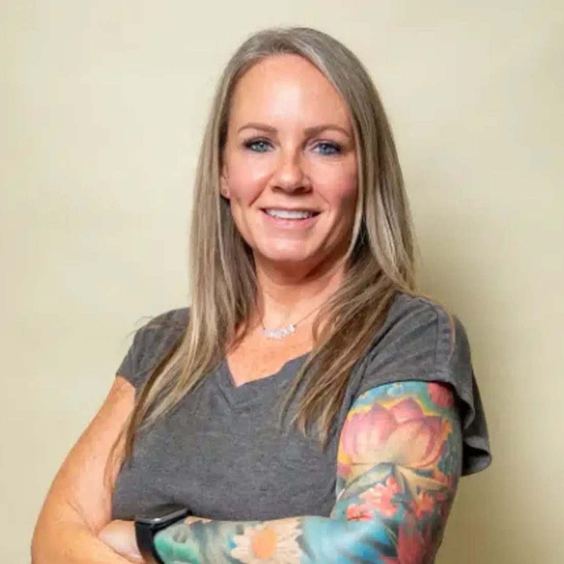 Smiling woman with tattooed arm in gray shirt against beige wall
