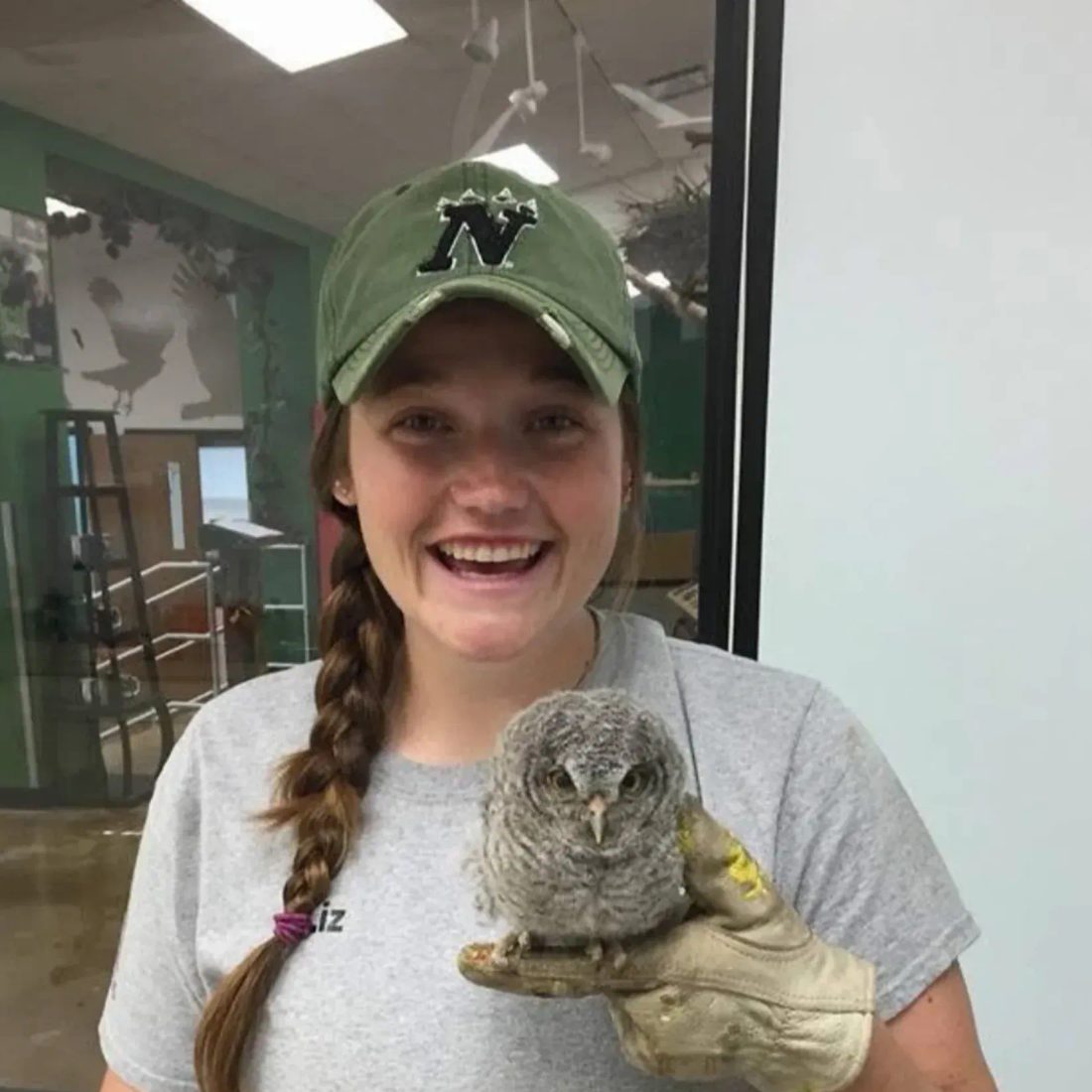 Woman in green cap holding a small owl on gloved hand
