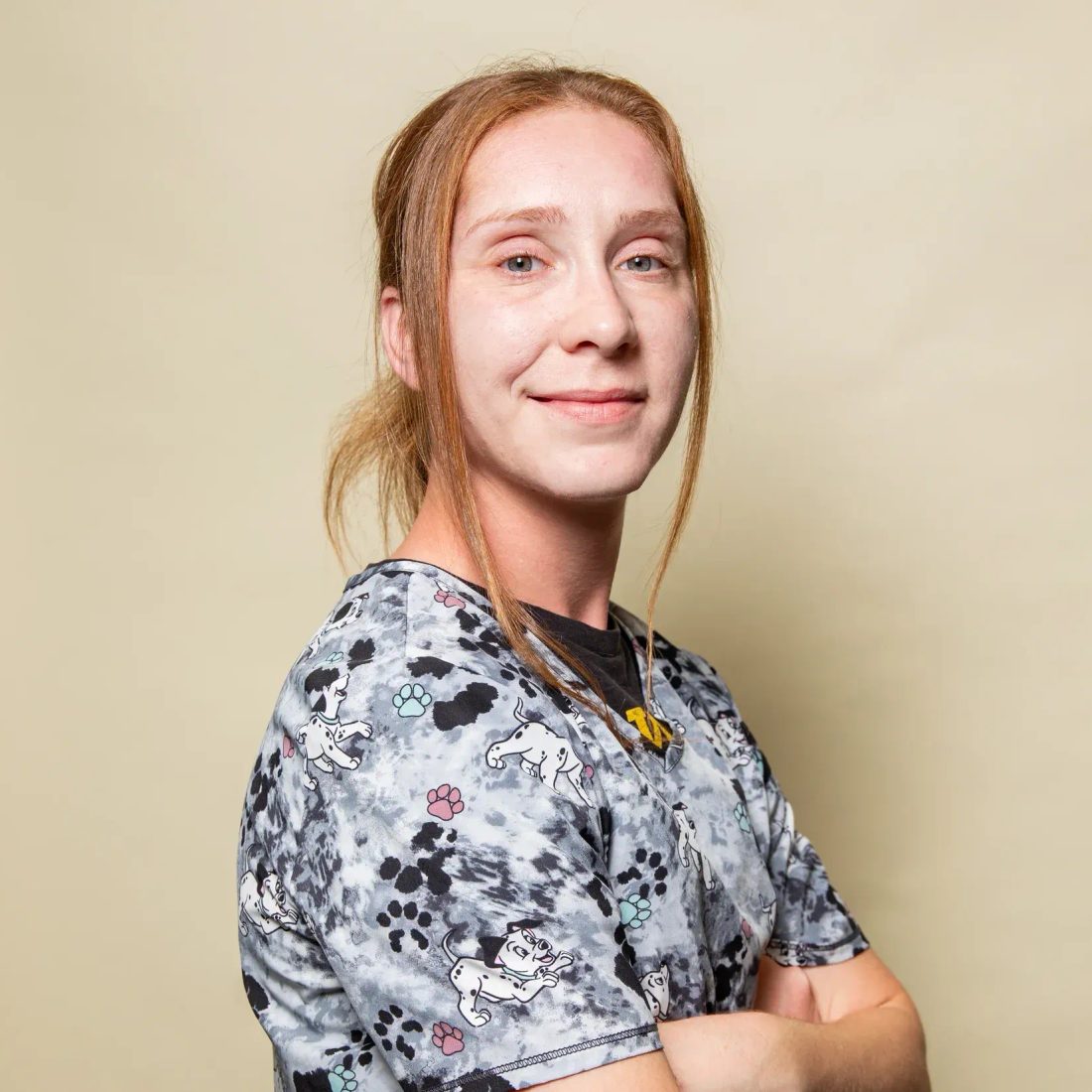 Woman in patterned scrub top with arms crossed smiling