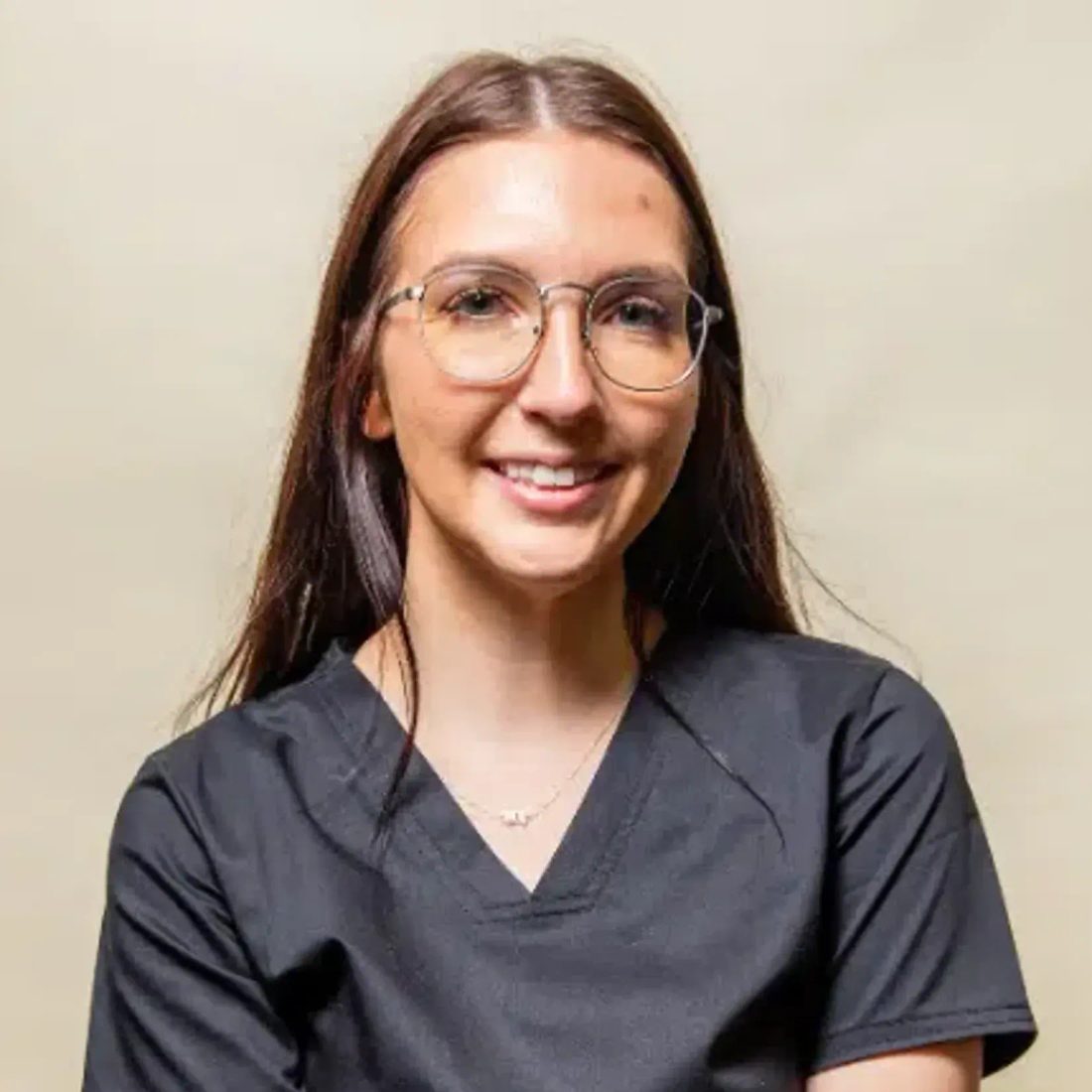 Young woman with glasses in black scrubs smiling at camera